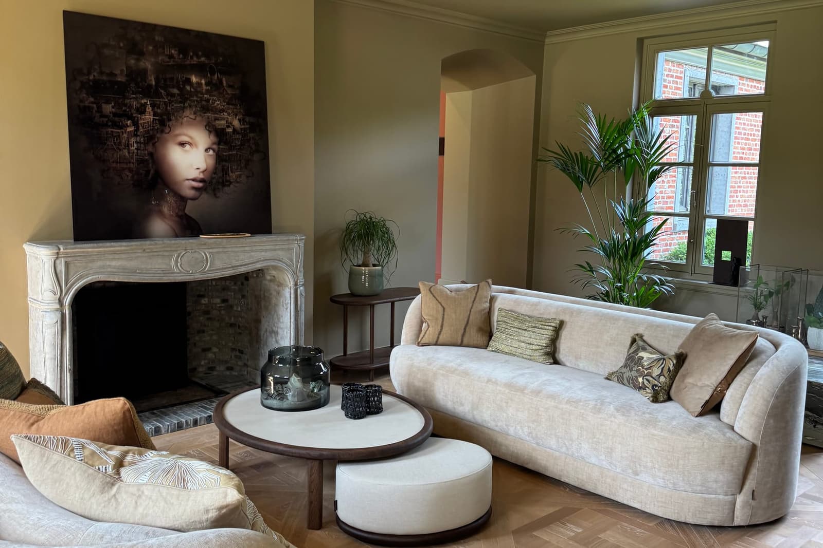 A living room with two curved sofas, an antique fireplace and a portrait above it